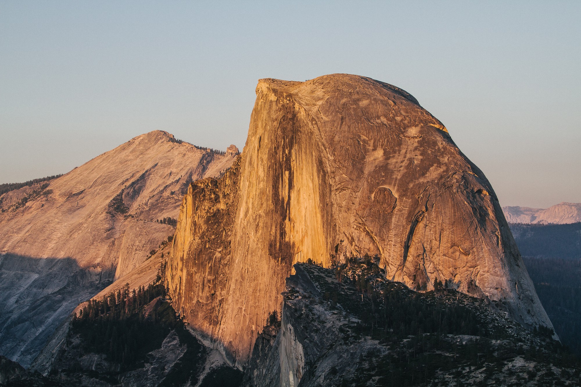 O Half Dome, um paredão de granito arredondado e cortado reto de um lado, iluminado de laranja pelo sol do fim da tarde